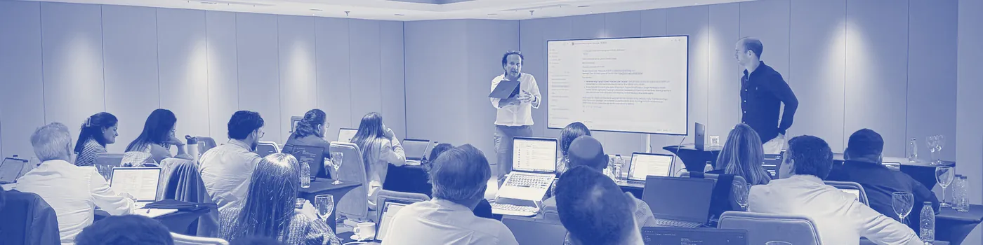 Sala de un taller vista desde el fondo: los dos instructores junto a la pantalla y los participantes con sus portátiles
